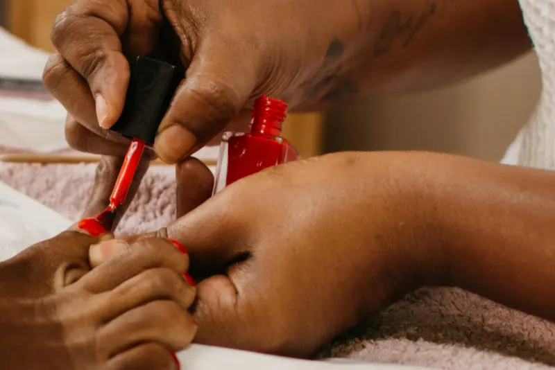 Pinceau de vernis rouge posé sur les ongles des pieds d’une cliente, à côté du flacon